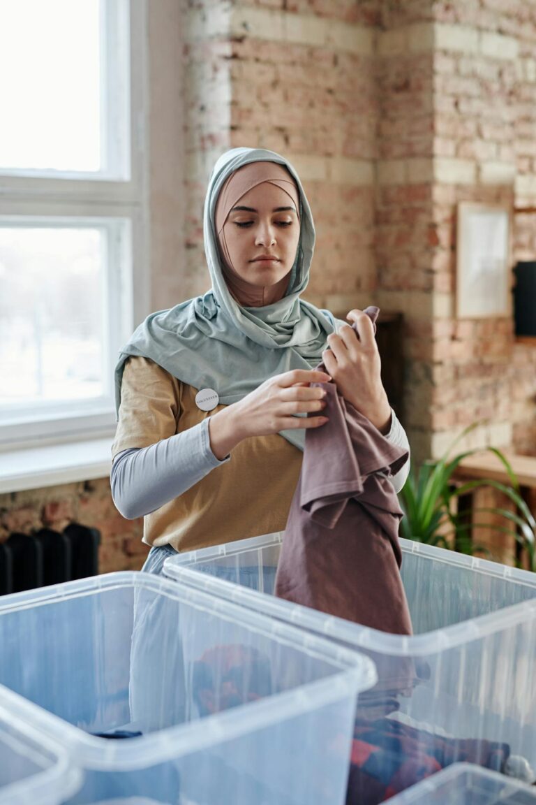 A woman wearing a hijab sorts clothing in a loft for donation purposes.